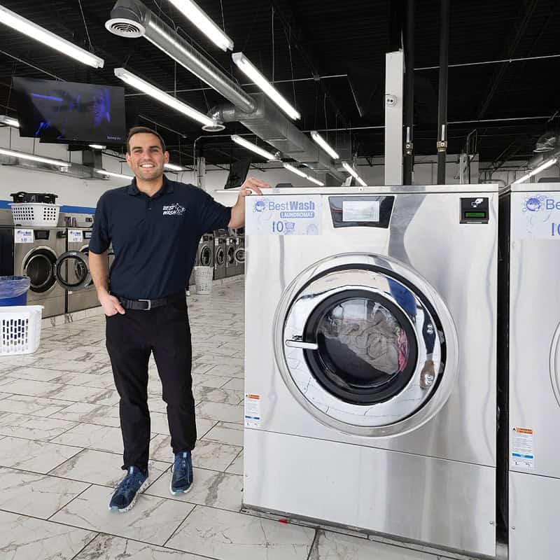 a man standing next to a washing machine in St Ann Laundromat at North Lindbergh, one of Best Wash Laundromats location